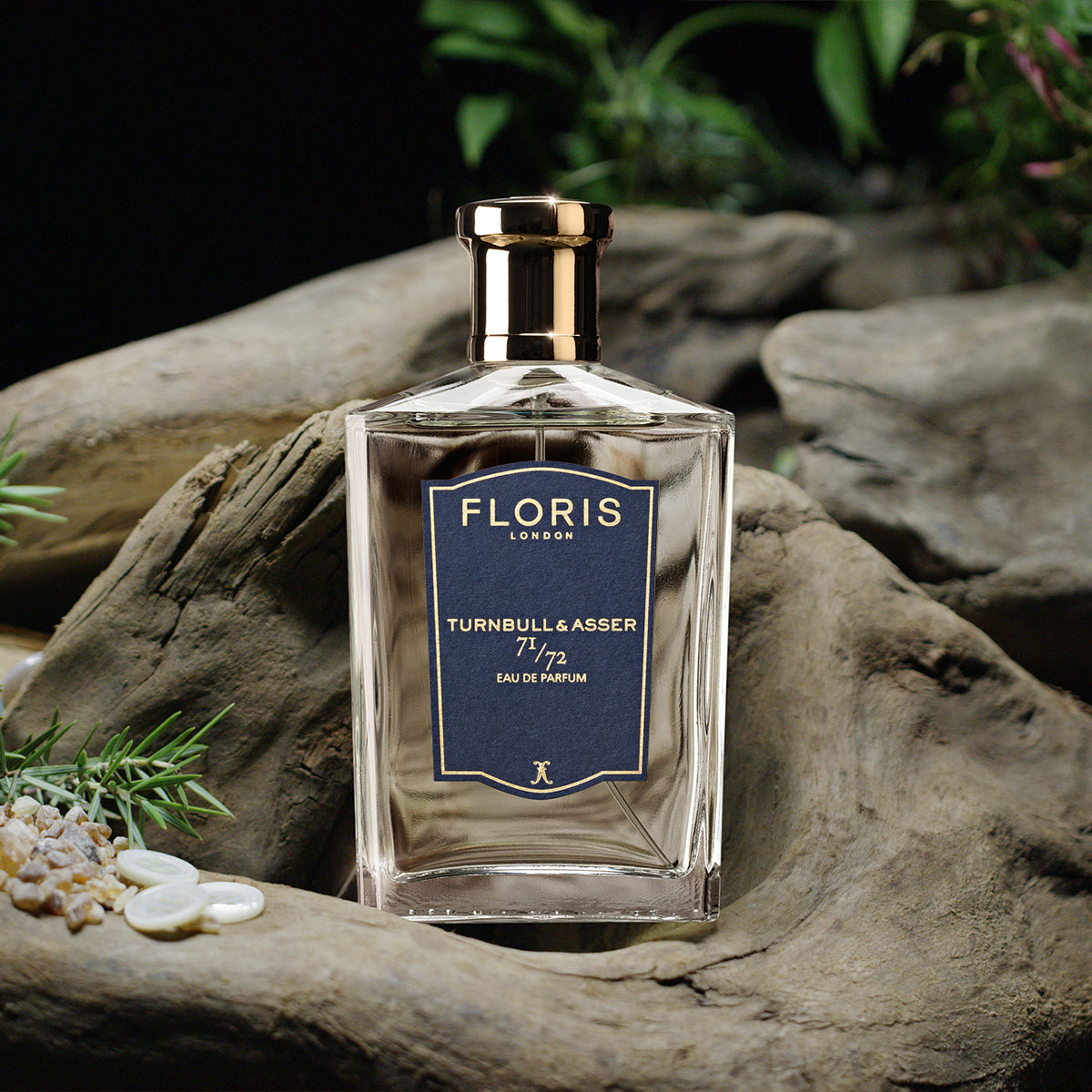 A Floris London 71/72 Eau de Parfum bottle rests on driftwood amid greenery and stones, evoking an air of refined woody fragrance.