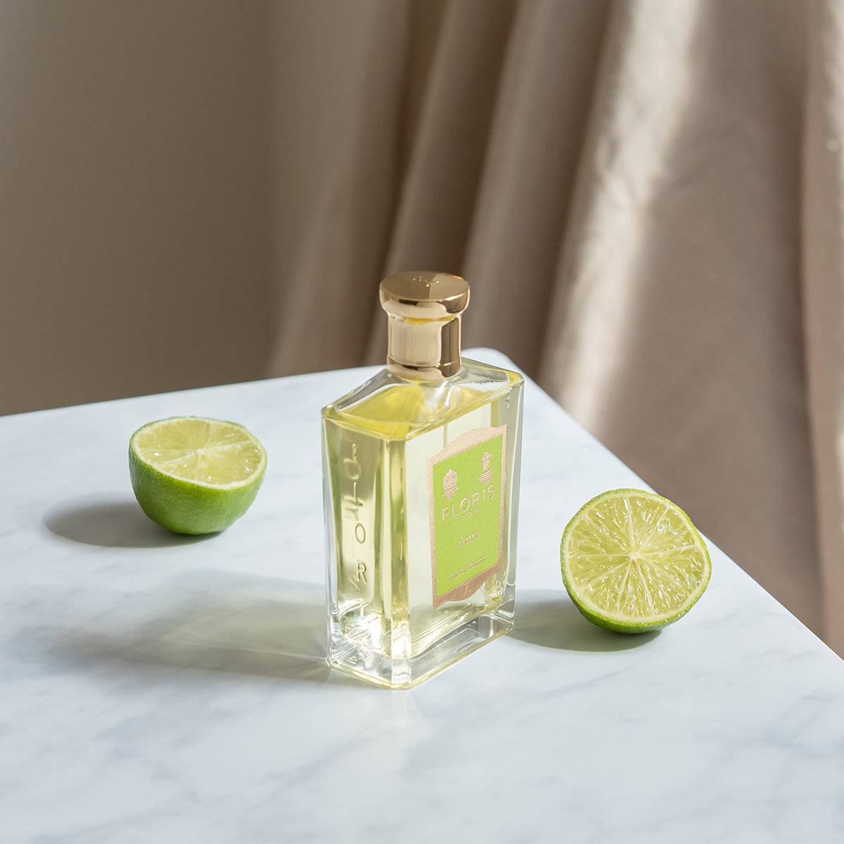 Floris London Limes - Eau de Toilette: a vegan citrus fragrance in an elegant bottle with gold cap, set on marble beside fresh halved limes.
