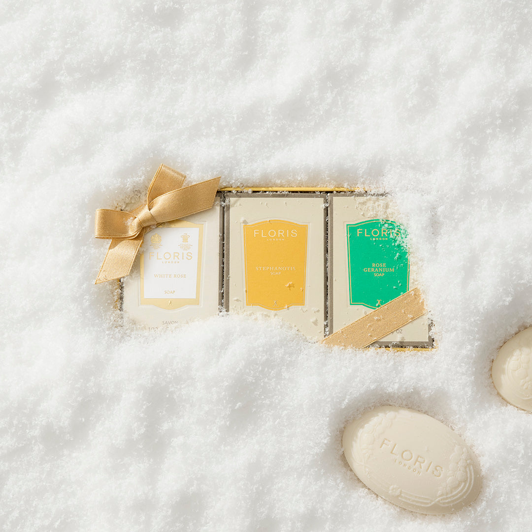 The Floris London Soap Collection | For Her gift box with gold ribbon and White Rose notes captures floral elegance amid snow and unwrapped bars.