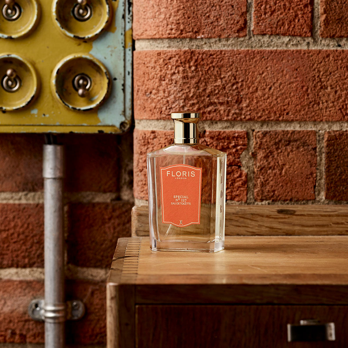 A bottle of Floris London Special No. 127 Eau de Toilette sits on wood by a brick wall, evoking British perfumery with citrus and floral fragrance notes.