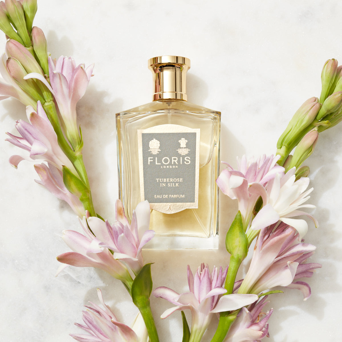 Floris London's 'Tuberose in Silk - Eau de Parfum' bottle amid jasmine, pink, and white flowers on marble, capturing its fragrant essence.