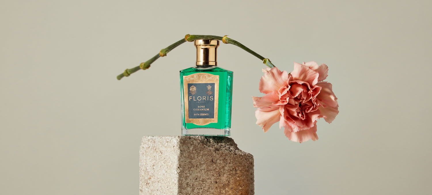 A bottle of Rose Geranium Bath Essence on a stone with a Rose overhanging the bottle