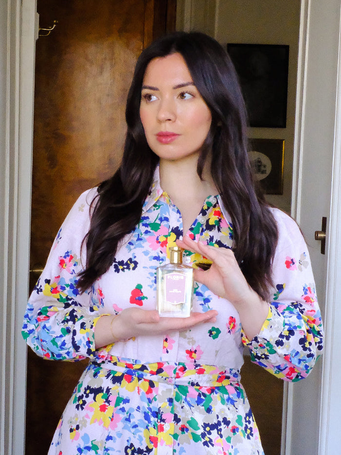 Joë of Curious Curation in a colourful shirt dress holding a bottle of Floris London Lily Eau de Toilette