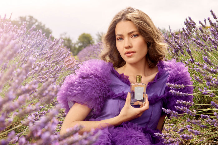 A woman in a purple dress holds Purple Mémoire - Eau de Parfum by Floris London UK, amid fragrant lavender blooms with hints of jasmine in the air.