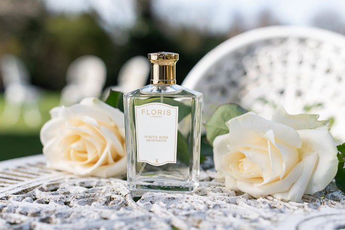 A bottle of White Rose on a white iron garden table surrounded by white roses.