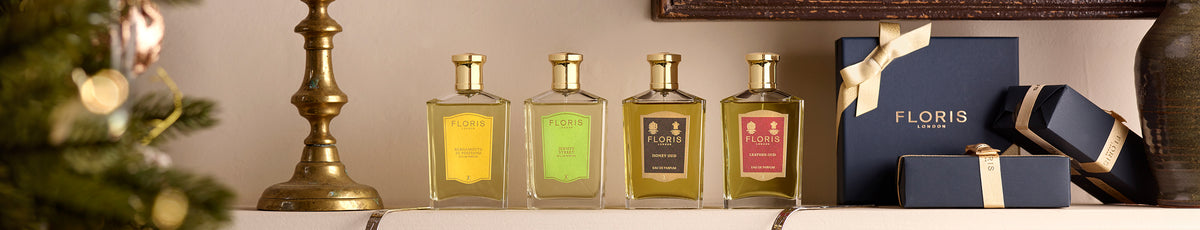 Bottle of perfume and wooden container with white soap placed on a rustic wooden surface, next to green leaves.