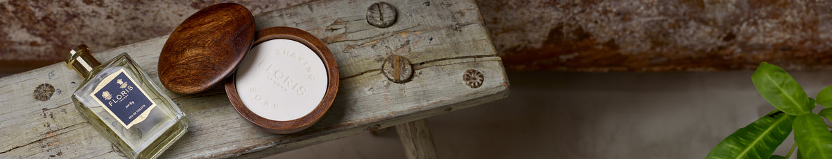 Perfume bottle and wooden soap container on a rustic wooden bench with a green plant nearby.