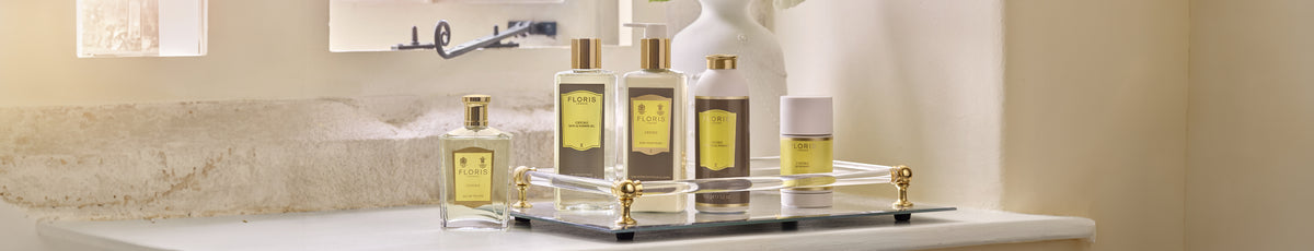 A set of luxury toiletries with gold labels on a tray, placed on a white countertop near a window.