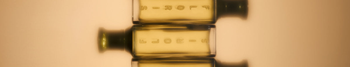 Three perfume bottles with green, orange, and yellow labels displayed on a shelf next to a framed painting.
