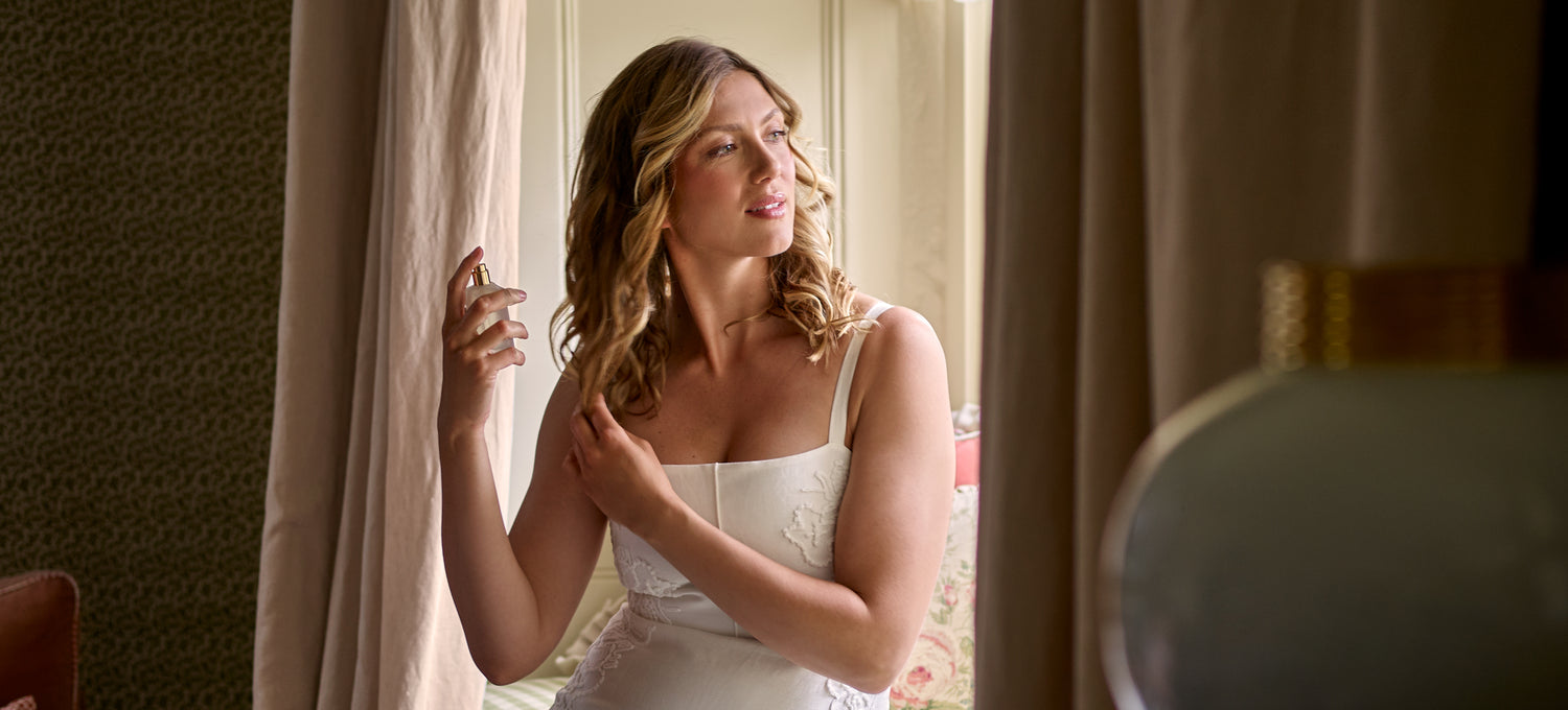 A woman sitting in front of a window, spraying her hair with Floris London Cherry Blossom Hair Mist.