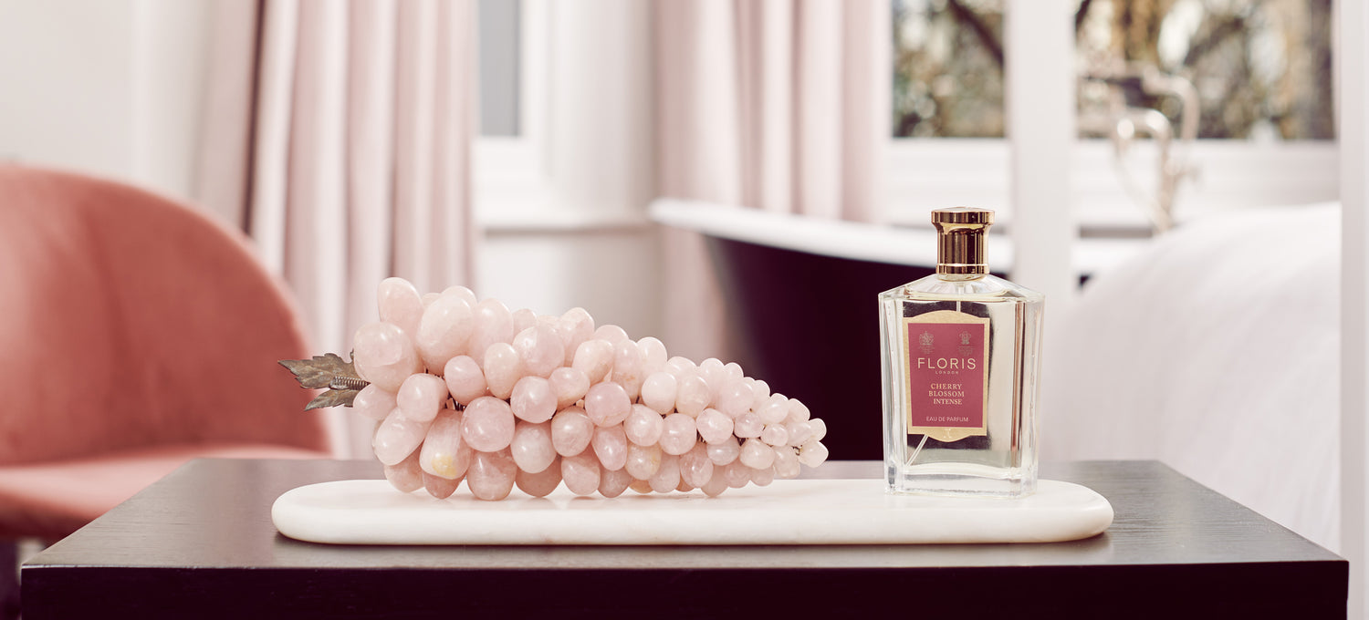 A pink background with Pink grapes and a bottle of Floris London Cherry Blossom Intense Eau de Parfum