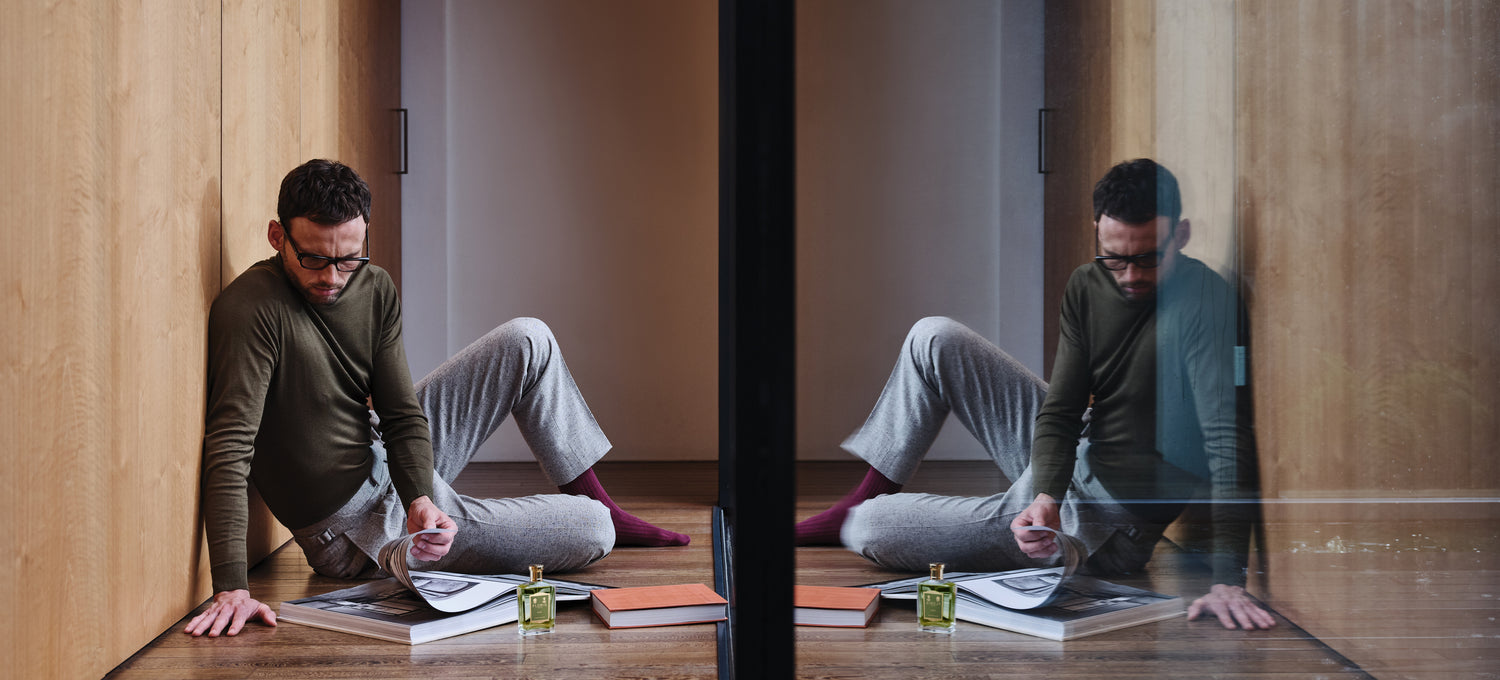 A man sitting on the floor reading a book, with a bottle of Elite in front of him.