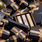 Gift boxes adorned with gold ribbons encircle a central box featuring the Floris London Perfumer's Trilogy: For Her in a luxurious setting, ideal for the season of celebration. Inside, explore exquisite floral fragrances designed to add a touch of elegance to any occasion.