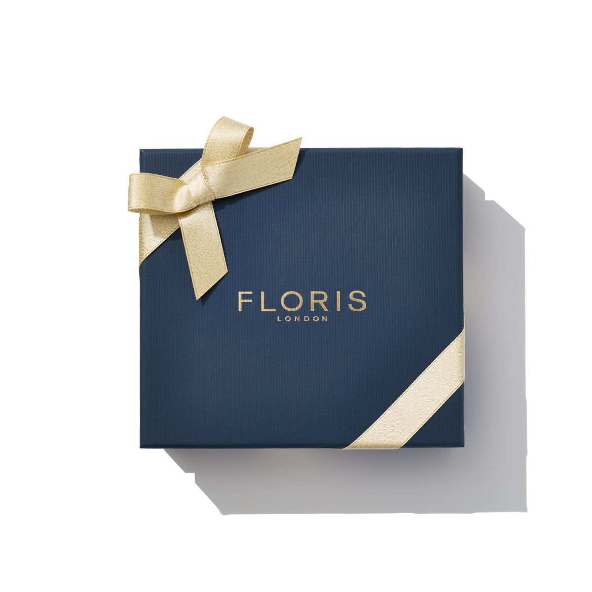 The "Perfumer's Trilogy: For Him" comes in a sophisticated dark blue gift box adorned with a gold ribbon and bow, featuring the brand name "Floris London" elegantly embossed in gold. This exquisite packaging, perfect for the festive season, encases premium British men's fragrances, making it an ideal gift for someone special.