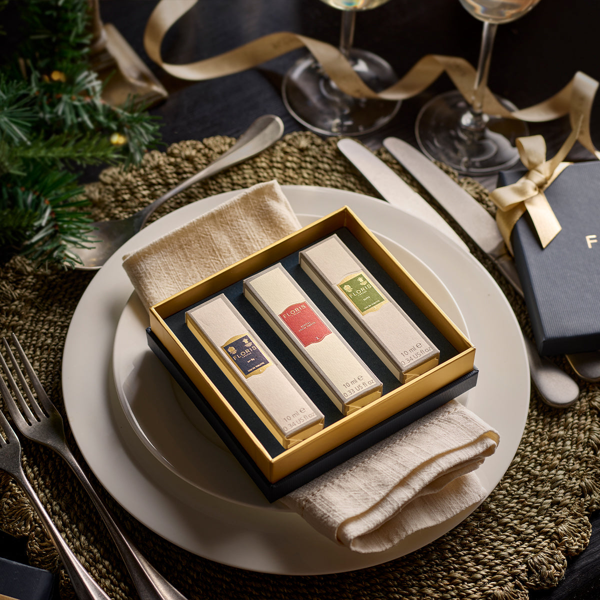 Perched elegantly on a dinner plate and accented by cutlery and festive decor, the Perfumer's Trilogy: For Him by Floris London is a gift box containing three rectangular packages. Perfect for the festive season, this is an ideal gift that embodies British men’s fragrances, adding an aromatic touch to your celebrations.