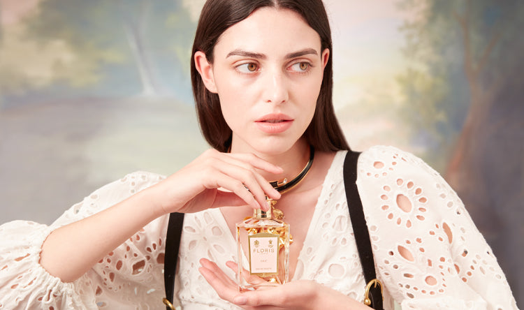 A woman wearing a lace top, holding a bottle of Lily perfume.