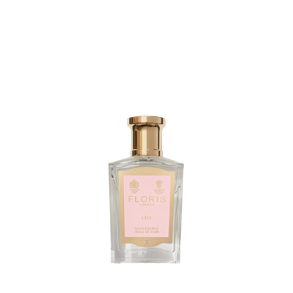 A transparent perfume bottle with a gold cap and pink label reads "Floris London Lily - Bath Essence," offering a delicate lily of the valley floral scent.