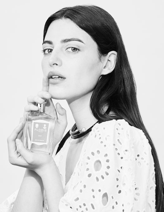 A model holding a bottle of perfume close to her face, her finger is up 
