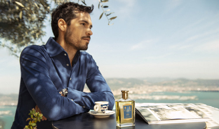 Man sat with a coffee and a bottle of Neroli Voyage with a Mediterranean background