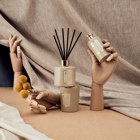 Wooden hands display Oud & Cashmere by Floris London, with candles, a diffuser, and dried flowers on a beige fabric background.