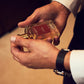 Man holding a Floris London Santal Eau de Toilette bottle, wearing a white shirt and black watch—the ideal men’s signature scent.