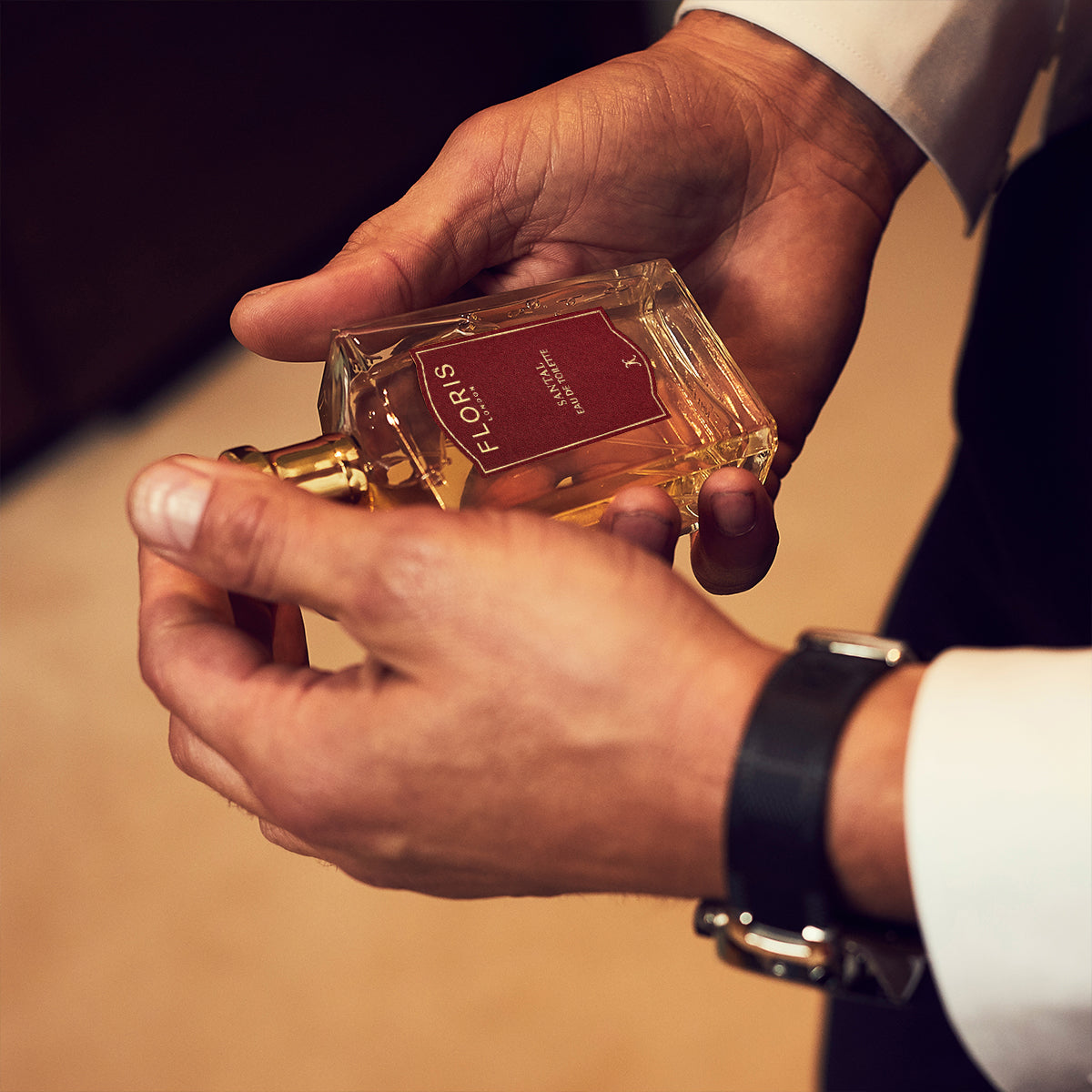 Man holding a Floris London Santal Eau de Toilette bottle, wearing a white shirt and black watch—the ideal men’s signature scent.