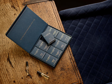 A Floris London UK Sample Set is open on a wooden table beside navy quilted fabric, displaying the brand’s signature fragrances.